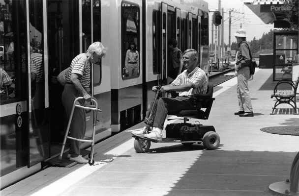 A woman using a walker exists a low-floor MAX car while a man in a motorized wheelchair boards