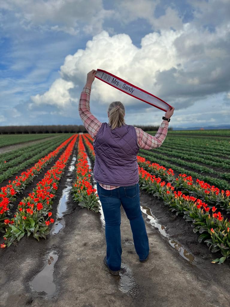 Photo of pageant winner Krista Stone holding her pageant banner in a field of tulips